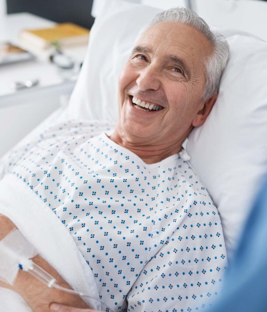 Elderly man in hospital bed and gown, smiling